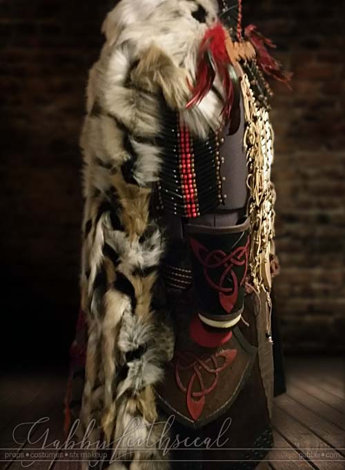 Right side view of black, white, ivory and red Beast costume with beaded chest plate, celtic bracers and fur cloak.