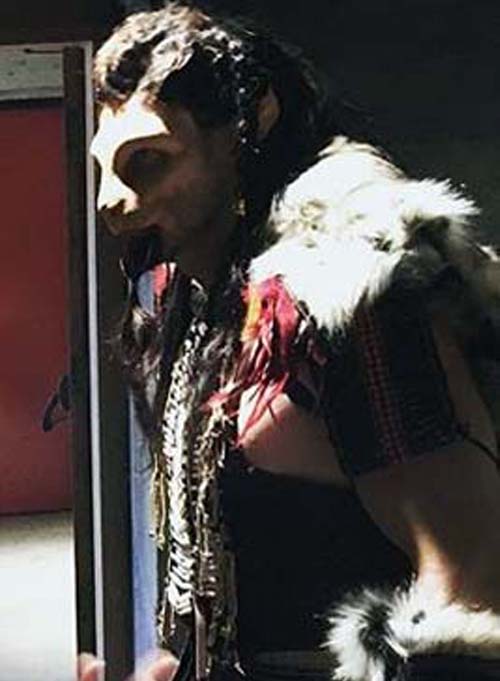 Man in harsh lightling wearing cat like prosthetic makeup in The Beast costume with black, white, ivory and red costume with beaded chest plate, celtic bracers and fur cloak.