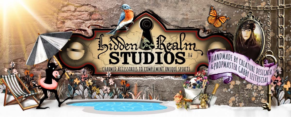 Hidden Realm Studios logo basks poolside on a bright summer day, surrounded by colorful flowers, birds, and butterflies. A pail holds pink and blue flowers around a skull, while a goblin shadow hides under a striped umbrella with a pink flamingo float.