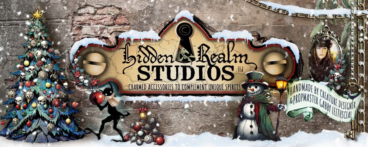 Hidden Realm Studios logo settled in a gothic, snowy xmas scene with black, red, green, and gold hues. There are skull-shaped ornaments, a snowman, glowing lanterns, and a playful goblin shadow decorating tree.